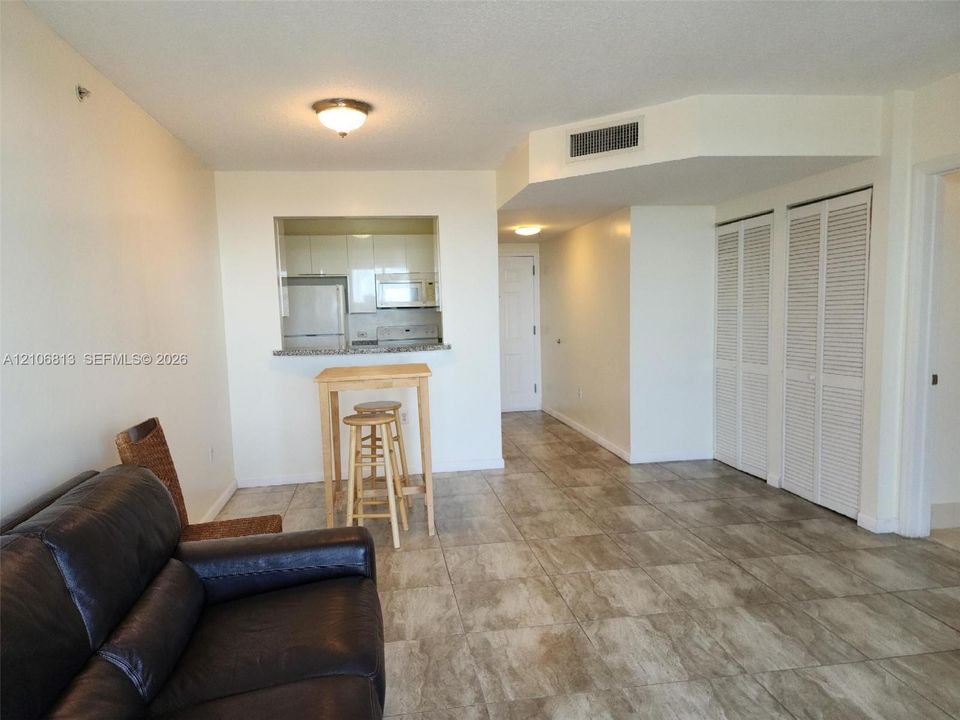 Open-concept interior featuring large-format stone-finish tile flooring, kitchen pass-through with stone countertop, and dual sets of louvered bifold closet doors