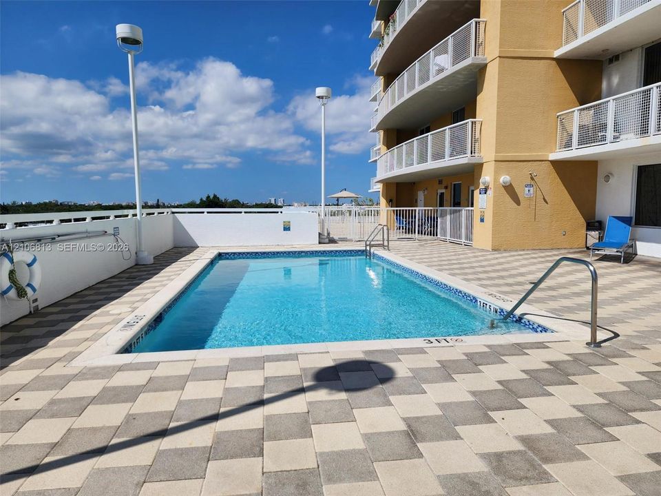 Outdoor swimming pool featuring a tiled deck, metal handrails, and a perimeter wall enclosure