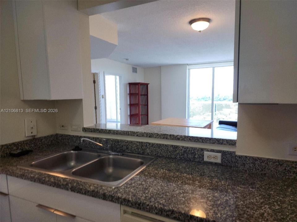 Kitchen featuring stone-finish countertops, dual-basin stainless steel sink, white cabinetry, and a pass-through window with an exterior window backdrop