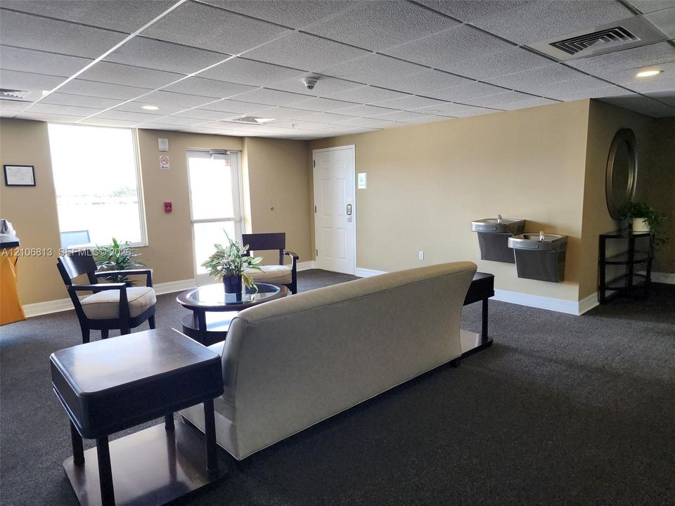 Common area featuring a drop ceiling with recessed lighting, wall-to-wall carpeting, dual wall-mounted water fountains, and a glass-paneled exterior door