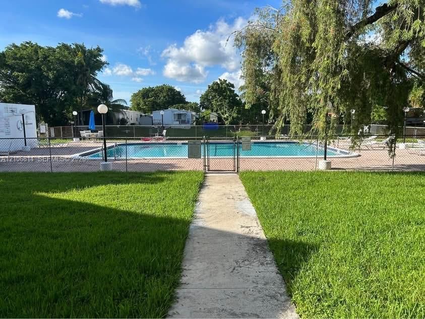 In-ground swimming pool surrounded by a concrete deck and enclosed by chain-link fencing, complemented by a manicured lawn and mature trees