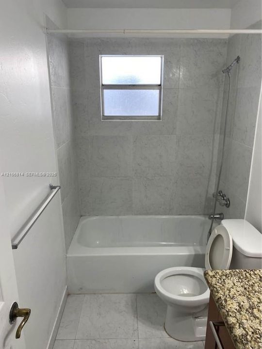 Bathroom featuring stone-finish countertop, tiled shower surround, integrated tub, and frosted window