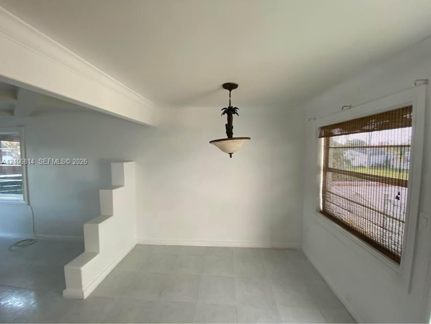 Interior space featuring a stepped architectural partition, neutral tile flooring, and a decorative pendant light fixture with a translucent shade