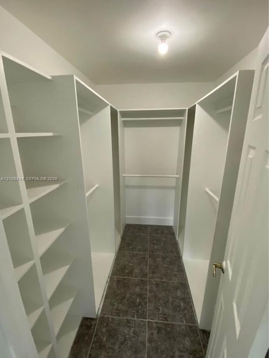 Walk-in closet featuring white built-in shelving, multiple hanging rods, and dark tile flooring