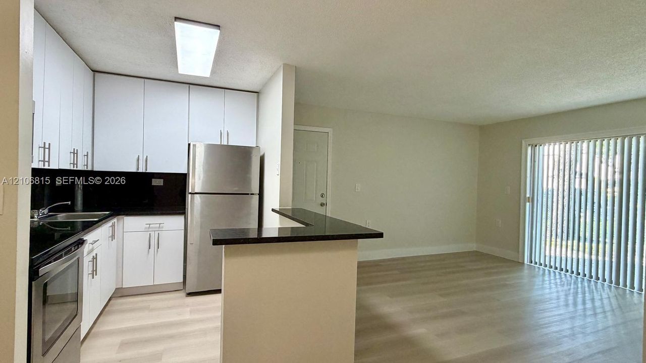 Kitchen featuring white cabinetry, dark countertops, a peninsula, stainless steel refrigerator, and wood-finish flooring