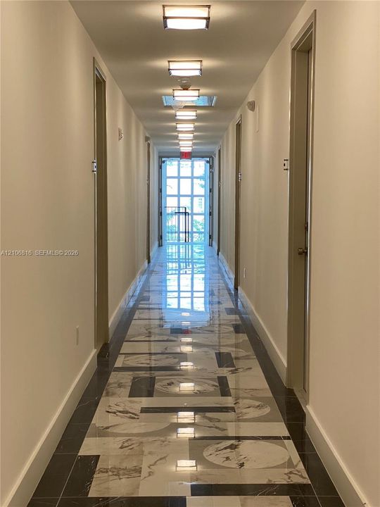 Hallway featuring geometric tile flooring with a high-gloss finish, flush-mount ceiling lighting, and a multi-pane glass door