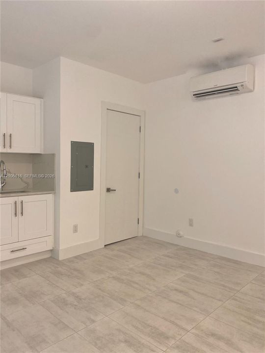 Kitchenette featuring white Shaker-style cabinetry, neutral stone-finish countertops, tile flooring, and wall-mounted air conditioning unit