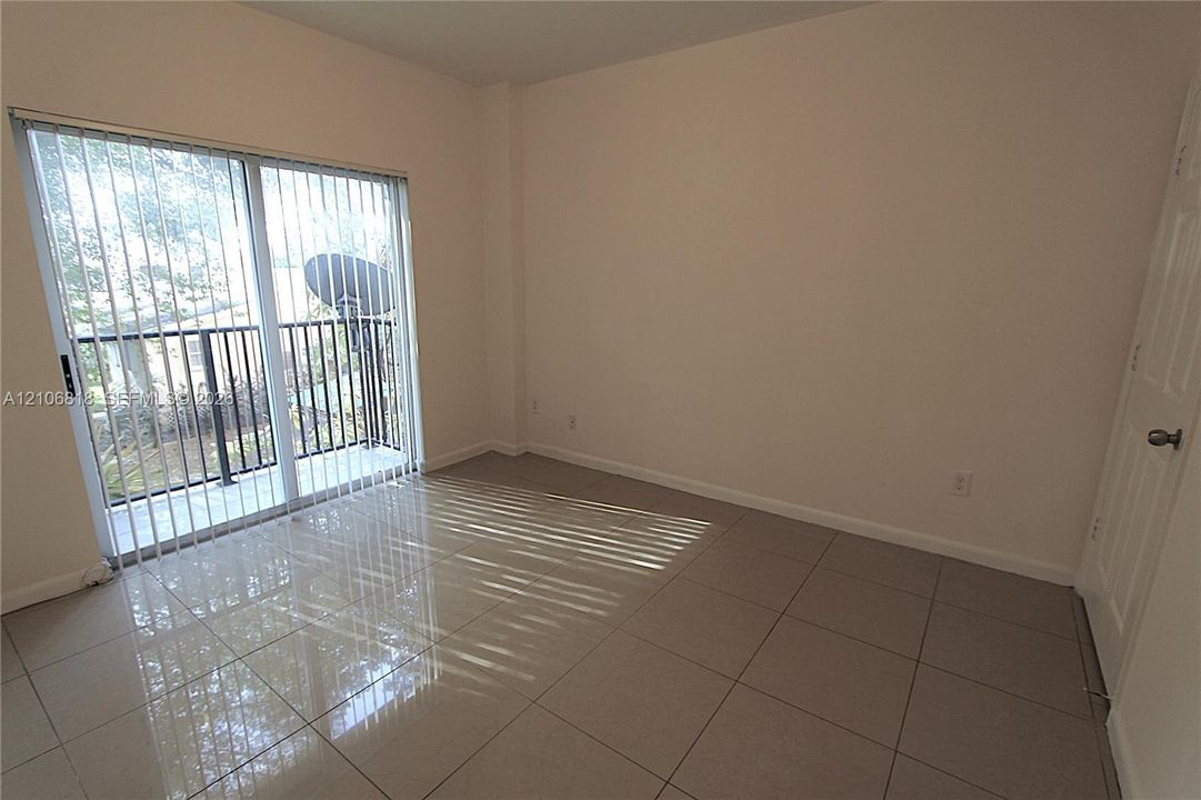 Neutral-toned room featuring large-format polished tile flooring, sliding glass door with vertical blinds, and a private balcony with black metal railing