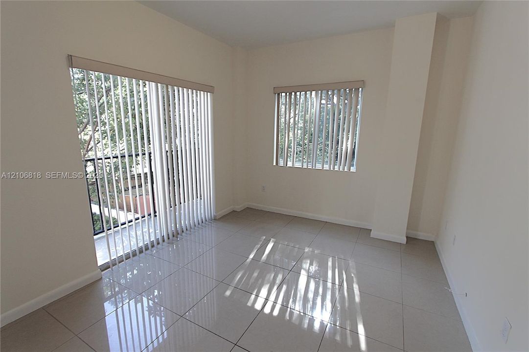 Neutral-toned tile flooring, large sliding glass door, vertical window blinds, and recessed wall design