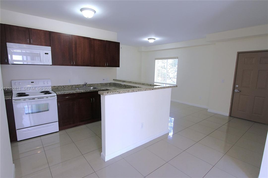 Kitchen featuring dark wood cabinetry, stone-finish countertops, tile flooring, white appliances, and a breakfast bar