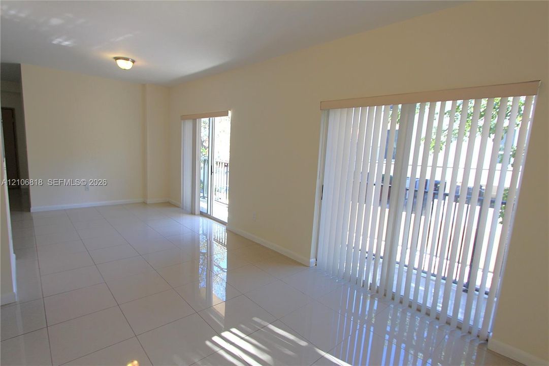 Large ceramic tile flooring, neutral wall tones, and dual sliding glass doors with vertical blinds