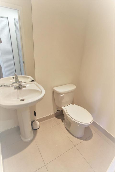 White porcelain pedestal sink with a chrome single-handle faucet, integrated wall-mounted mirror, and tile flooring