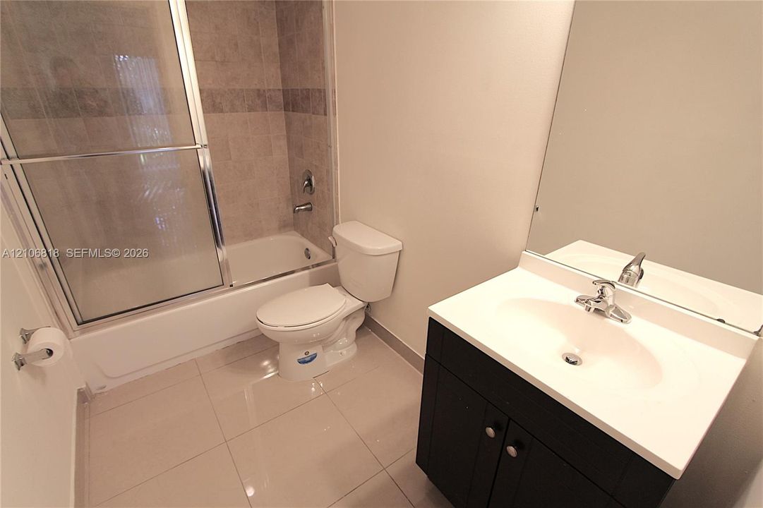Bathroom featuring a vanity with a white countertop and dark cabinetry, large wall mirror, and a tub-shower combination with sliding glass doors and tiled surround