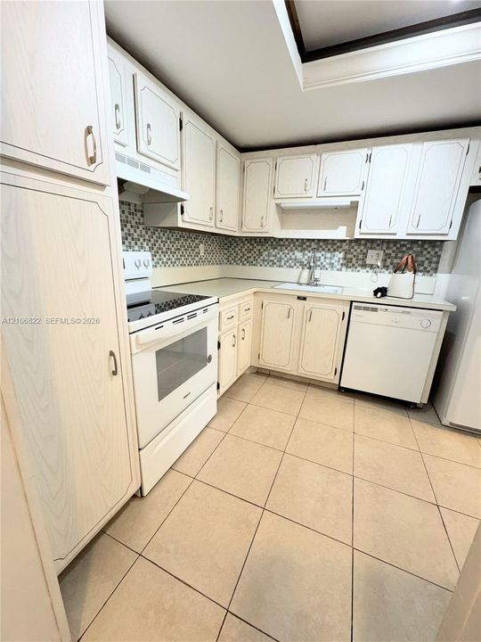 Kitchen featuring off-white cabinetry, patterned mosaic tile backsplash, integrated white appliances, and large-format tile flooring