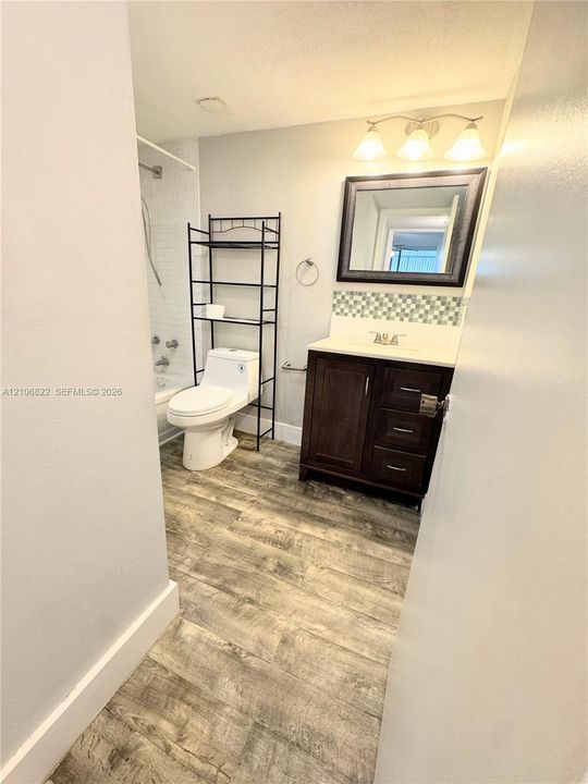 Bathroom featuring wood-finish flooring, dark-stained wood cabinetry, decorative mosaic tile backsplash, and three-light vanity fixture