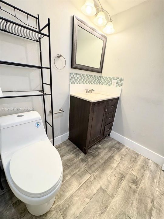 Dark-finish vanity with a rectangular sink, patterned glass mosaic backsplash, wood-finish flooring, and a framed mirror