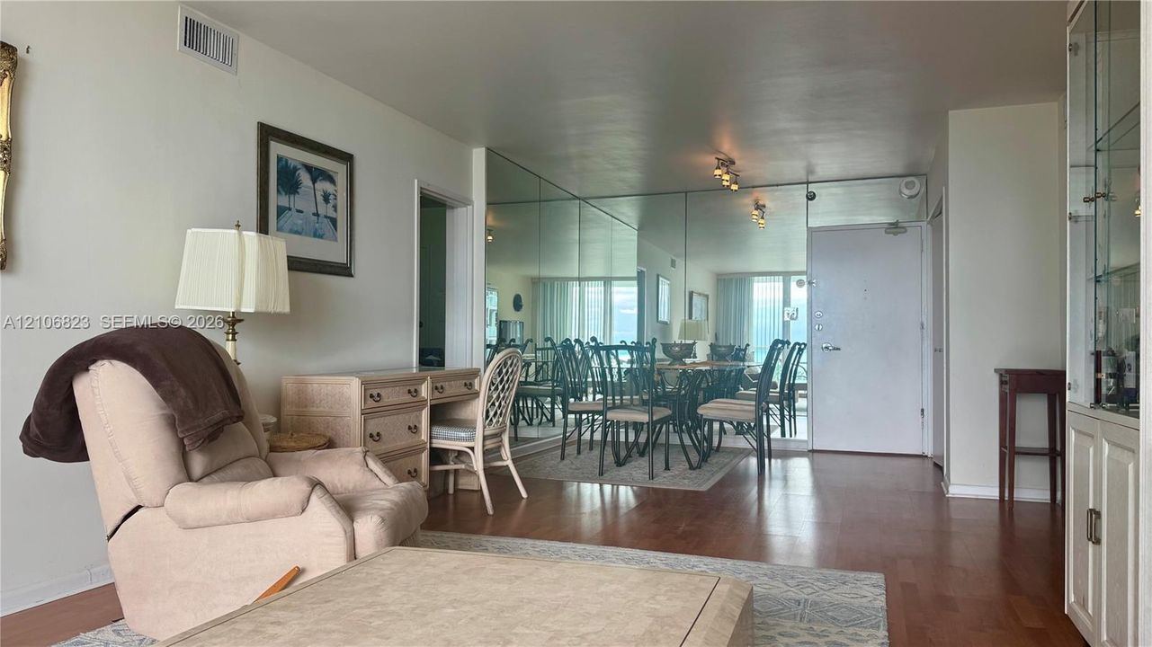 Living area featuring wood-finish flooring, floor-to-ceiling wall mirror, and built-in glass-front cabinetry