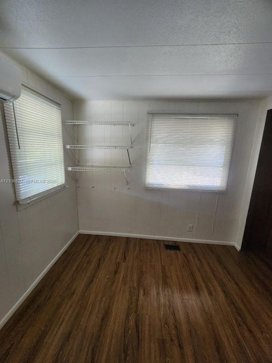 Wood-finish flooring, two windows with horizontal blinds, and three tiers of white wall-mounted wire shelving