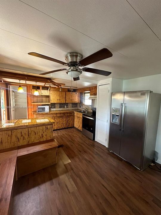 Kitchen featuring wood-finish cabinetry, tile backsplash, stainless steel side-by-side refrigerator, peninsula counter, and wood-finish flooring