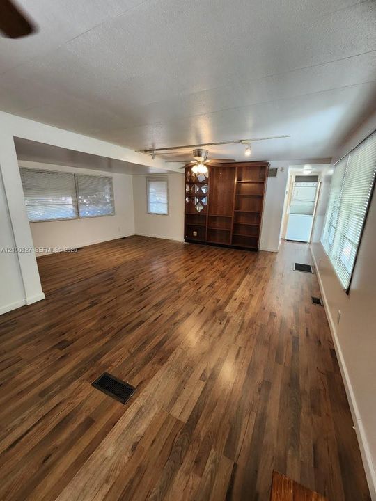 Living area featuring wood-finish flooring, built-in wooden shelving, a ceiling fan, and horizontal window blinds
