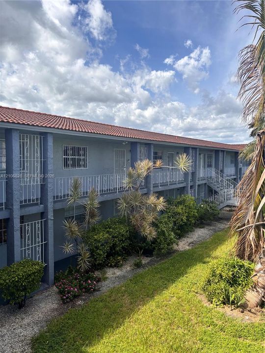Multi-story exterior featuring a clay tile roof, stucco siding, integrated metal railings, and established landscaping