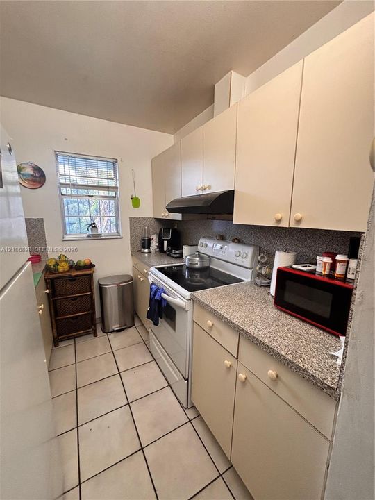 Kitchen featuring ample cabinetry, stone-texture laminate countertops, ceramic tile flooring, and a window providing natural light