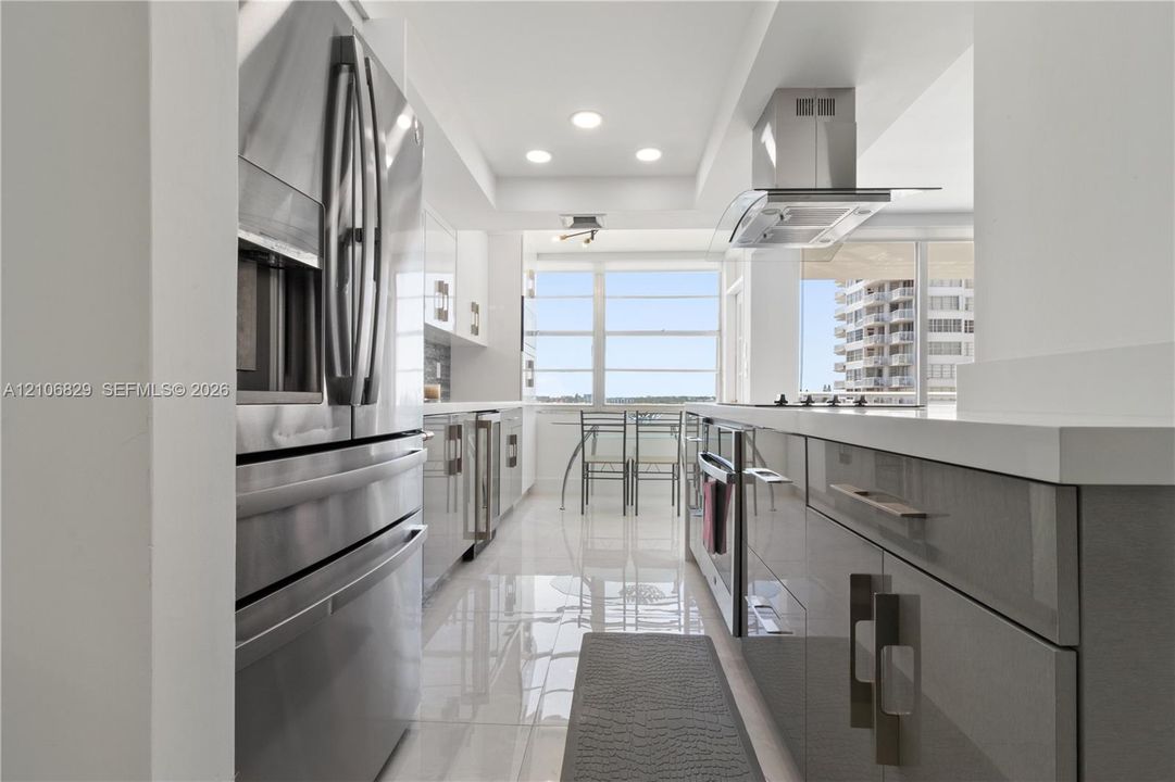 Kitchen featuring high-gloss cabinetry, stainless steel appliances, a stainless steel range hood, quartz countertops, and polished tile flooring