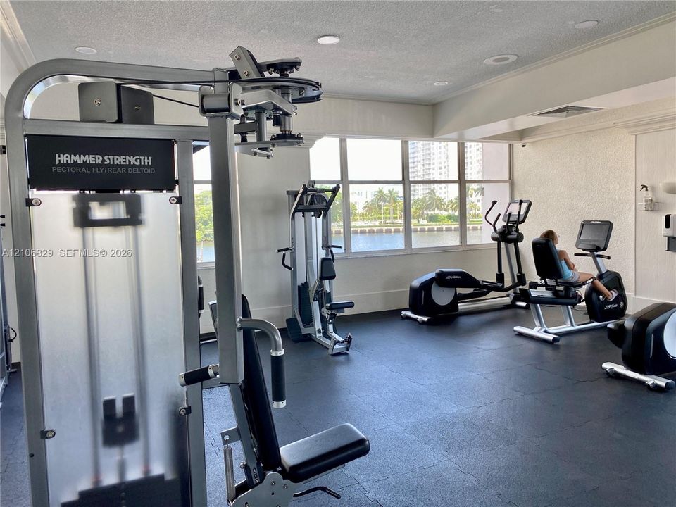 Fitness room featuring high-impact rubber flooring, expansive windows with water exposure, and recessed lighting