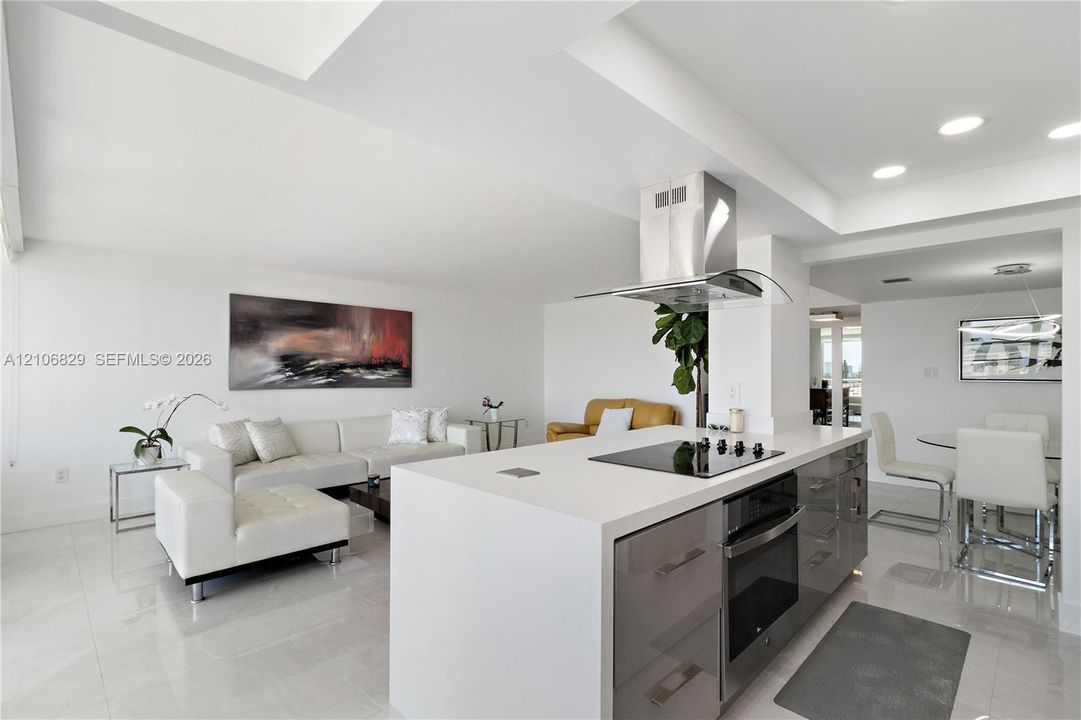 Kitchen island featuring stone countertops, integrated electric cooktop, stainless steel ventilation hood, and high-gloss cabinetry