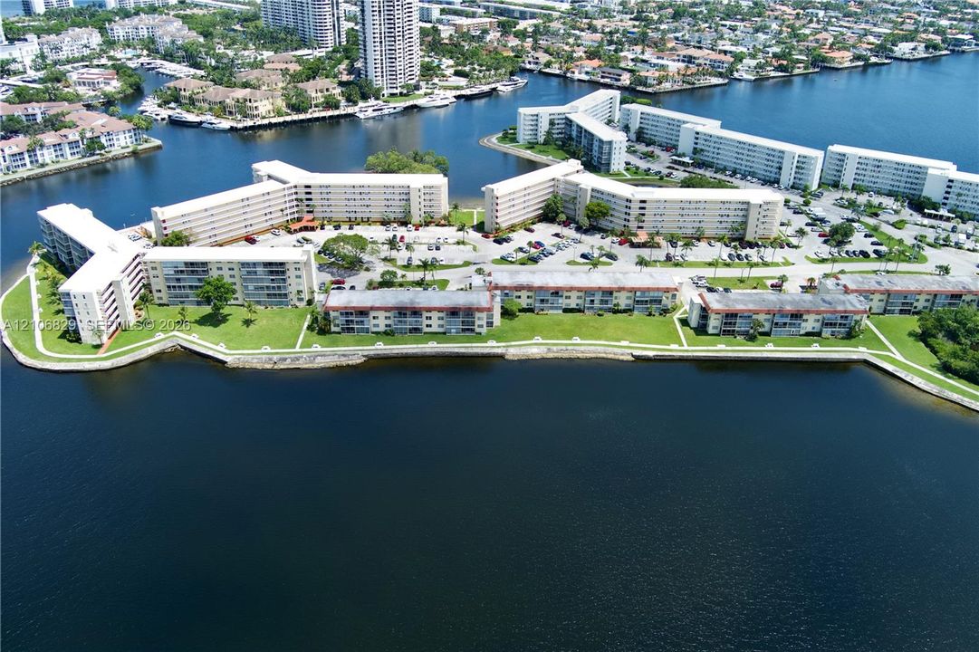 Waterfront residential complex featuring expansive canal frontage, multi-story buildings, paved parking areas, and manicured green space