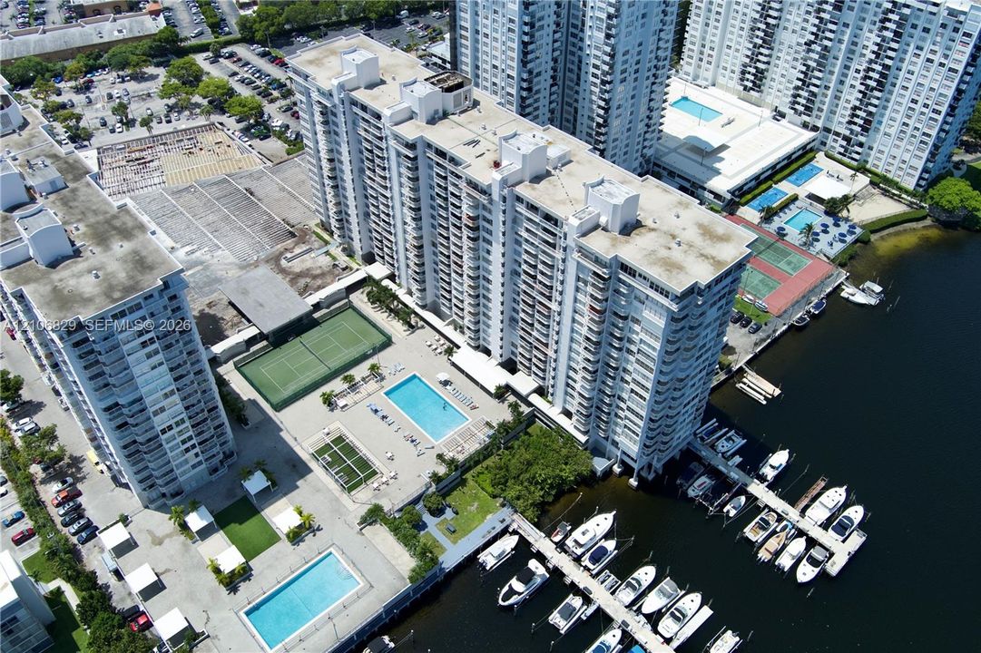 High-rise residential complex featuring waterfront boat slips, multiple outdoor swimming pools, tennis courts, and covered parking facilities