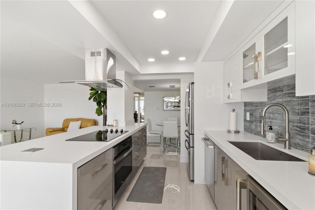 Modern kitchen featuring flat-panel cabinetry, solid-surface countertops, a stainless steel range hood, glass-tile backsplash, and recessed lighting