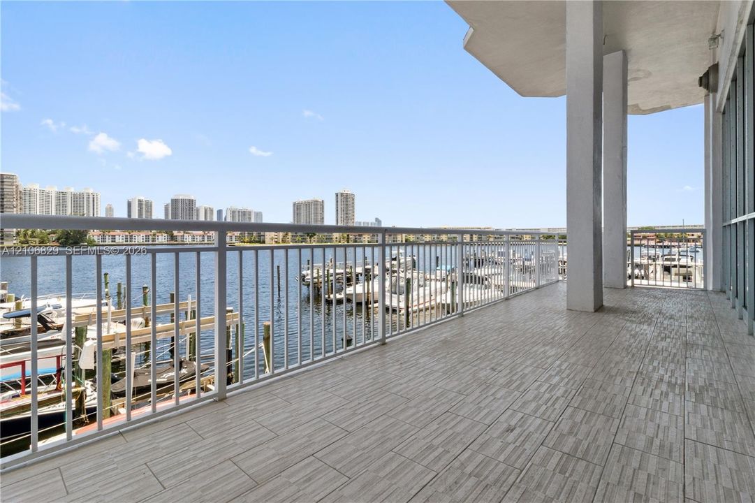 Covered balcony featuring wood-finish tile flooring, white structural pillars, and a metal railing overlooking a waterway with boat slips