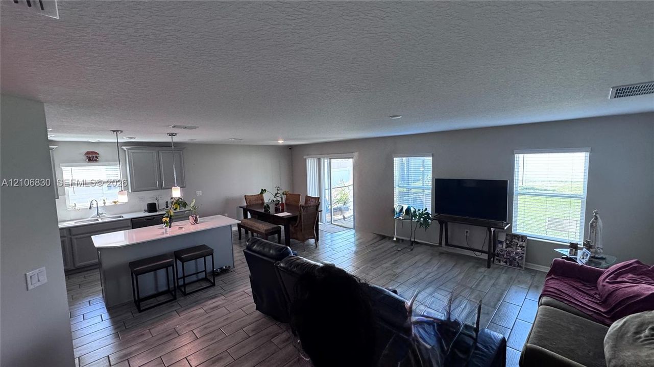 Open-concept kitchen and living area featuring wood-finish tile flooring, a kitchen island with quartz countertops, gray cabinetry, recessed lighting, and sliding glass doors