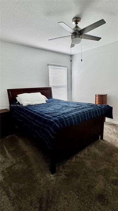 Neutral-toned walls, plush wall-to-wall carpeting, brushed-nickel ceiling fan with integrated lighting, and horizontal window blinds