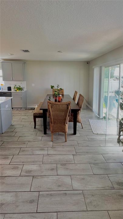 Open-concept interior featuring wood-finish tile flooring, recessed lighting, neutral-toned kitchen cabinetry, and sliding glass doors