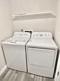 Laundry area featuring a top-loading washing machine, clothes dryer, and wall-mounted white shelving over wood-finish flooring