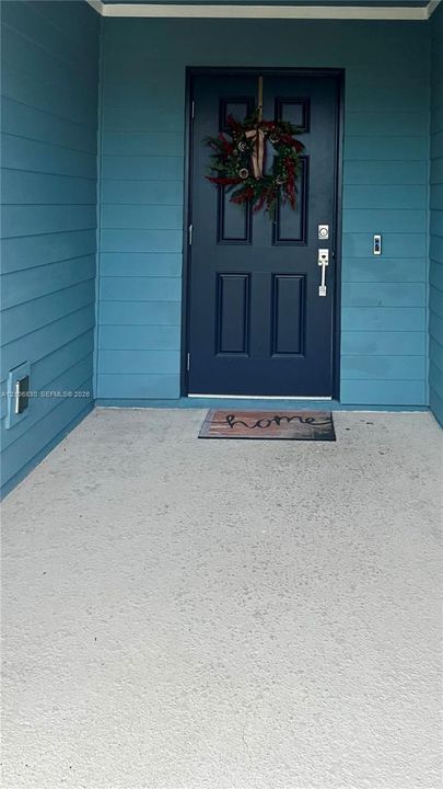 Covered entryway featuring blue lap siding, a solid-paneled door with brushed metal hardware, and a concrete porch