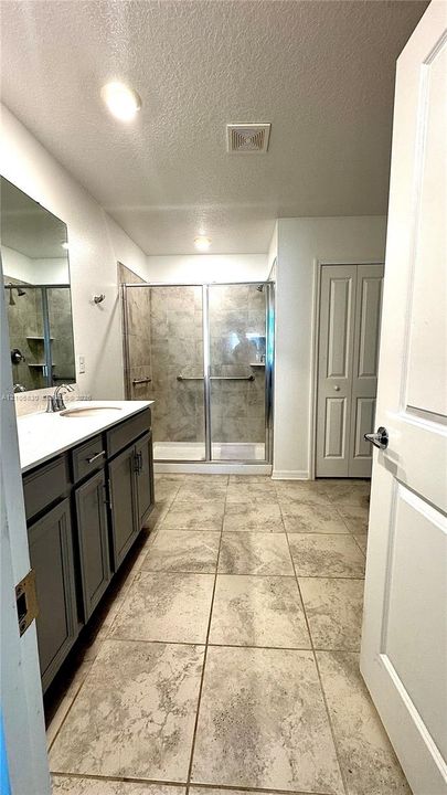 Bathroom featuring a dual-door vanity with a white countertop, walk-in shower with tile surround and glass enclosure, and large-format tile flooring