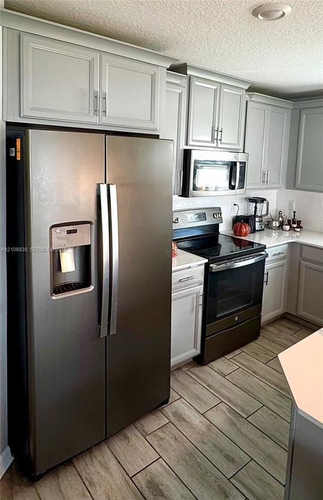 Kitchen featuring shaker-style cabinetry, stainless steel appliances, white solid-surface countertops, and wood-finish tile flooring