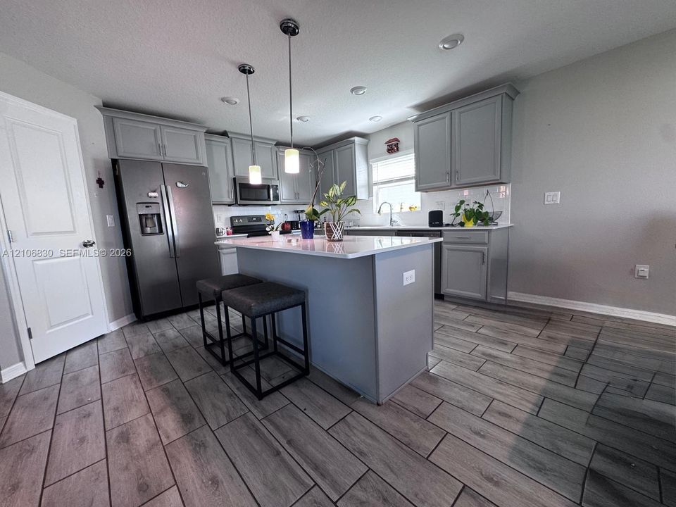 Kitchen featuring gray shaker-style cabinetry, central island with stone-finish countertop, stainless steel refrigerator, recessed lighting, and wood-finish tile flooring