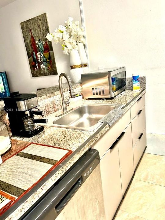 Kitchen area featuring stone-look countertops, flat-panel cabinetry with linear hardware, a stainless steel undermount sink, a high-arc gooseneck faucet, and an integrated stainless steel dishwasher