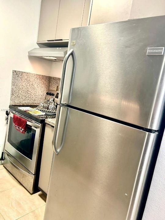 Stainless steel refrigerator and range, stone-composite backsplash, and neutral-toned cabinetry