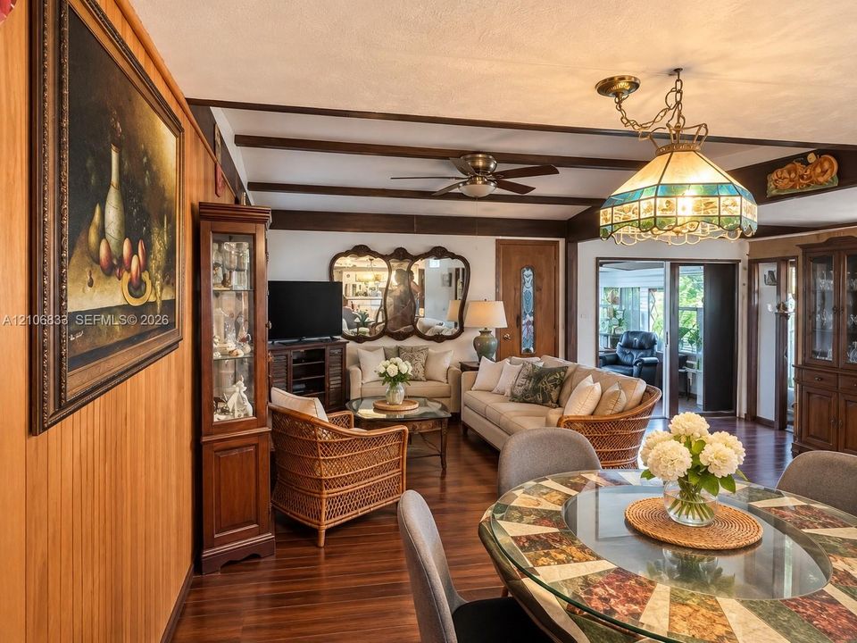 Wood-finish flooring, exposed ceiling beams, stained wood wall paneling, stained glass hanging light fixture, and integrated ceiling fan