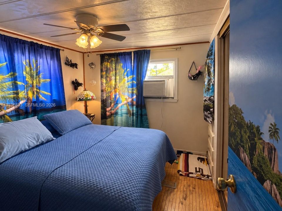 Room featuring wood-finish flooring, a ceiling fan with integrated lighting, and a wall-mounted air conditioning unit