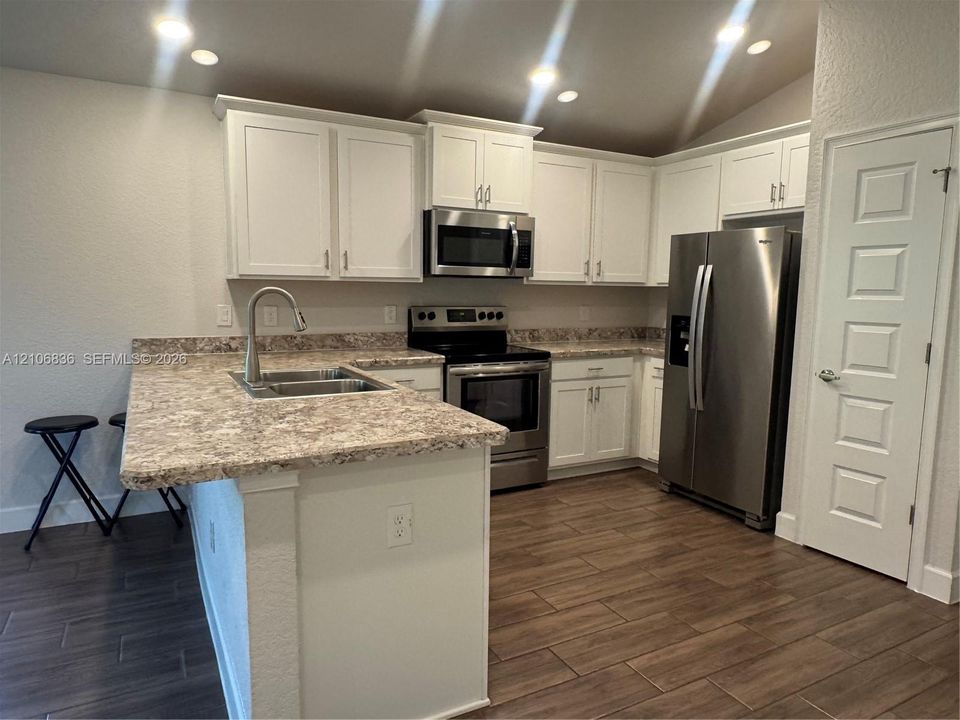 Kitchen featuring white cabinetry, stone-patterned countertops, stainless steel appliances, a high-arc kitchen faucet, and wood-finish tile flooring