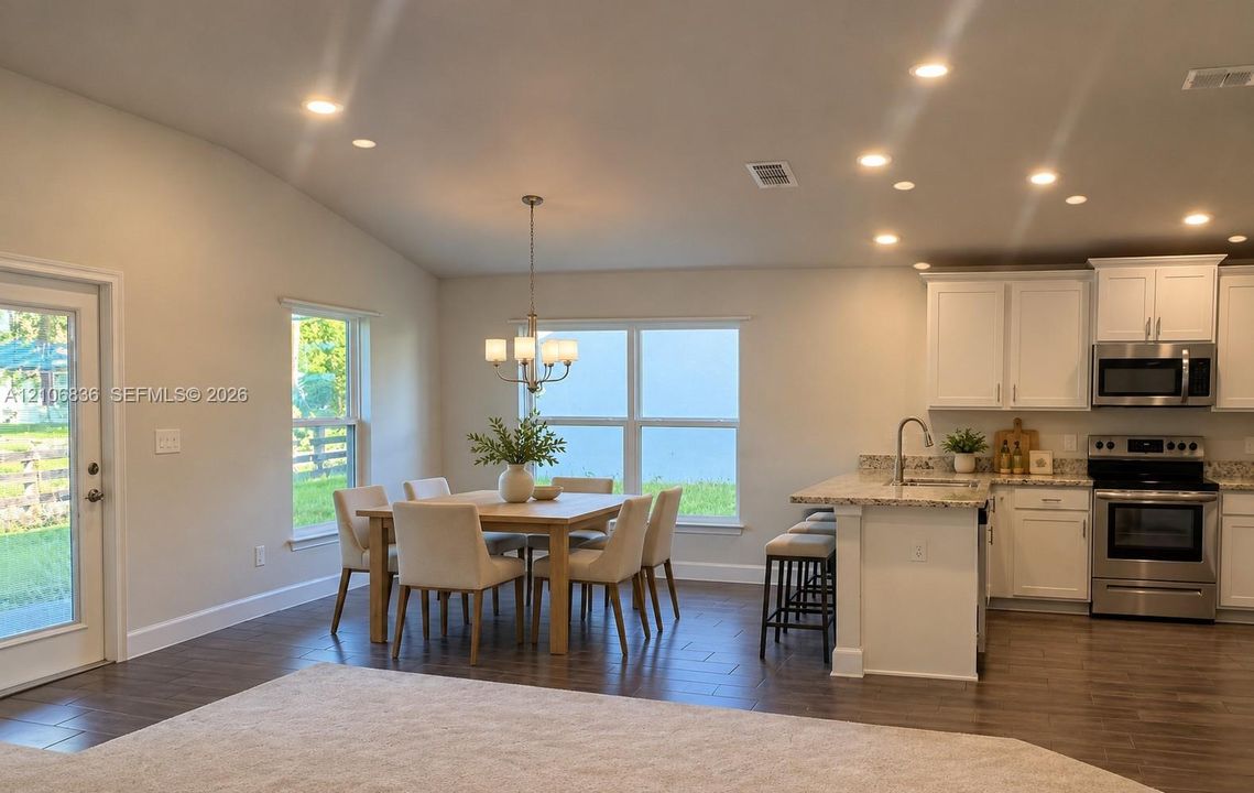 Open-concept kitchen and dining area featuring vaulted ceilings, recessed lighting, wood-finish flooring, white shaker-style cabinetry, and stone-surface countertops