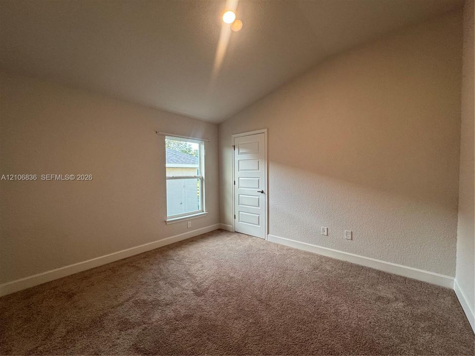 Vaulted ceiling featuring neutral-toned carpeting, five-panel interior door, and single-pane window