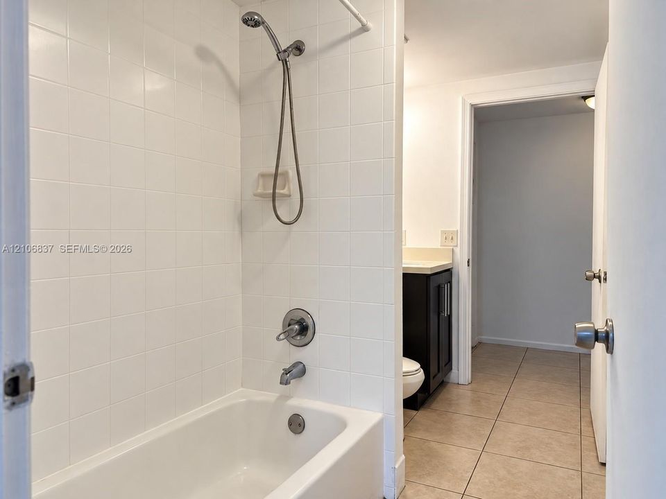 Bathroom featuring white tile surround, tub-shower combination with handheld fixture, dark wood-finish vanity with countertop, and ceramic tile flooring