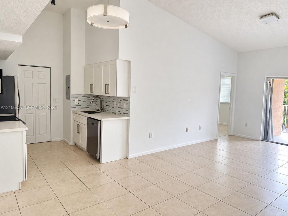 Kitchen featuring white cabinetry, solid-surface countertops, multi-toned tile backsplash, vaulted ceilings, and ceramic tile flooring